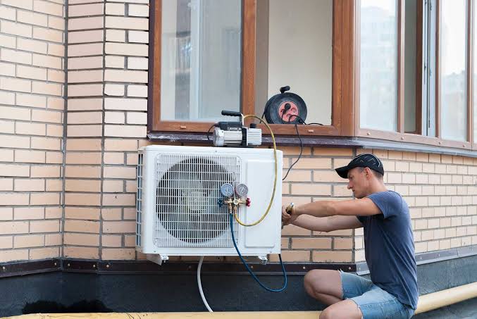 Technician connecting gauges to a wall-mounted outdoor heat pump unit